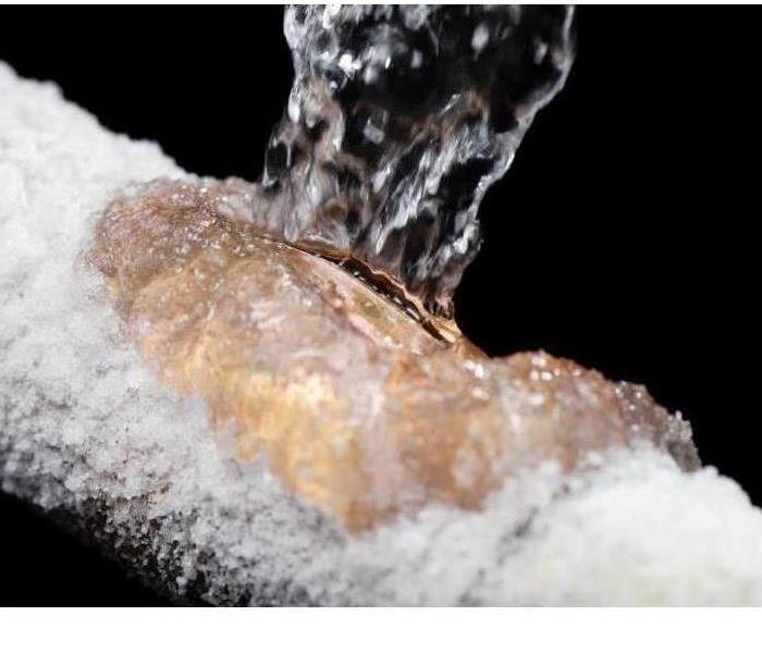 A frozen pipe with a slit in the pipe with water bursting out of the pipe.